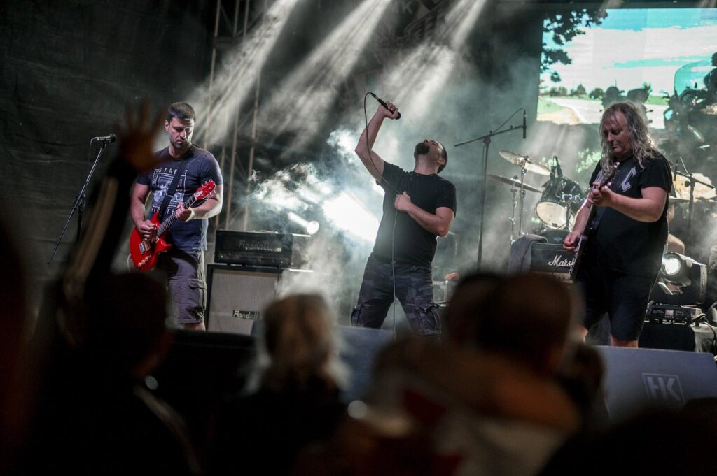 Musicians showcase their talent on stage during an outdoor festival, surrounded by dramatic lighting and a lively audience immersed in the music. The