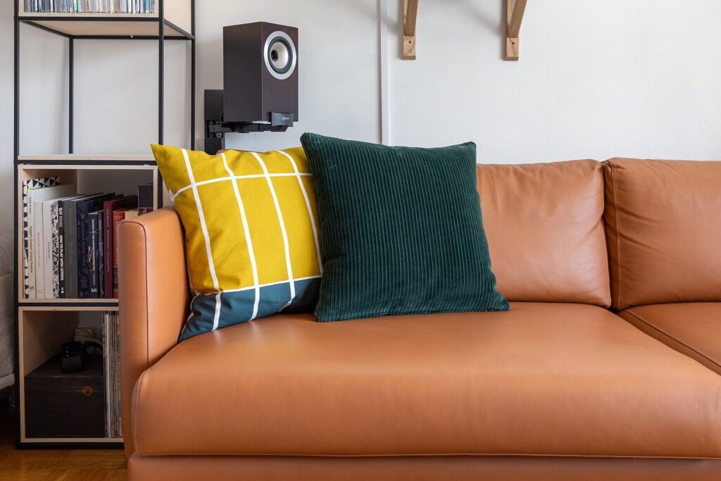 Almofadas customizadas em casa: 8 técnicas com e sem costura Decorative pillows on a leather sofa. A narrow bookshelf made out of plywood and steel and a Tannoy speaker on wall mount. Marimekko pillow and custom