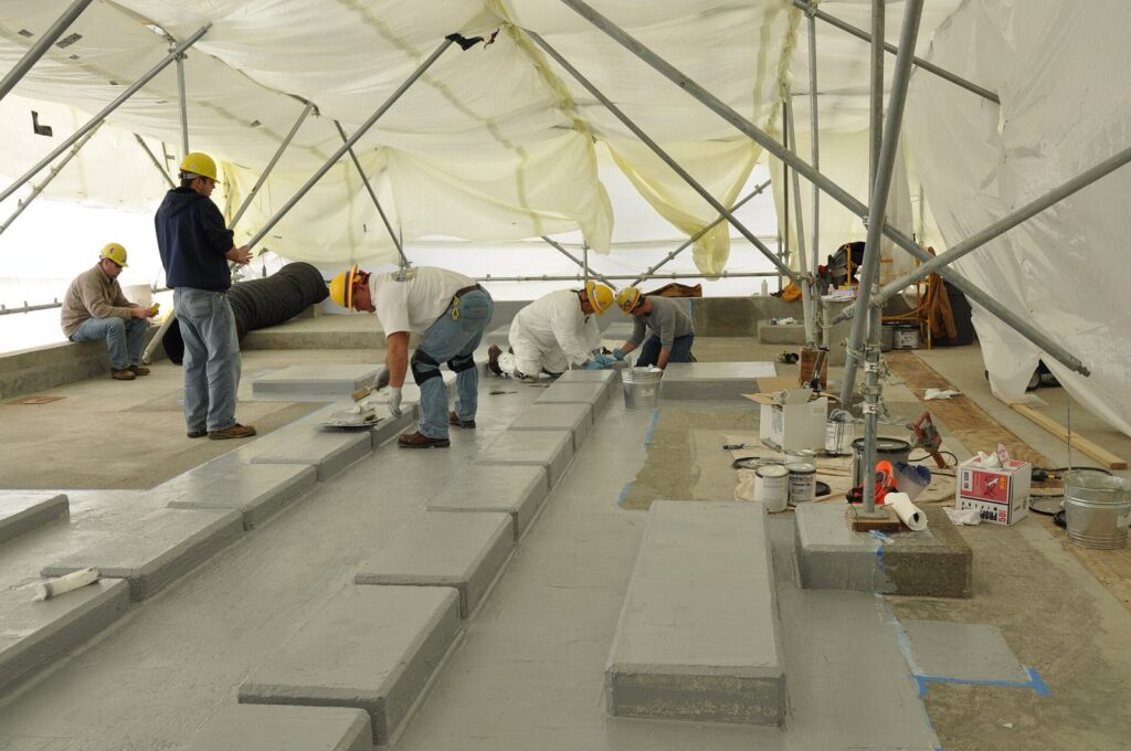 Tinta para Piso: Descubra o Segredo para Escolher a Certa em 2026 Workers place an epoxy coating on the floor of the Munitions Demilitarization Building.